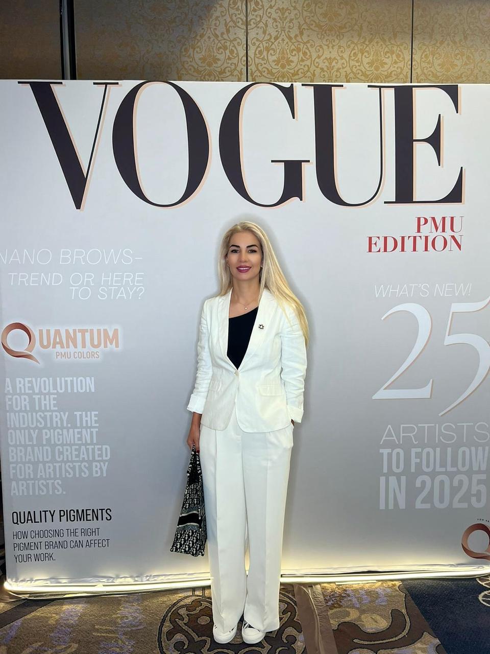 Roya standing in front of the Vogue PMU Edition backdrop at an industry event